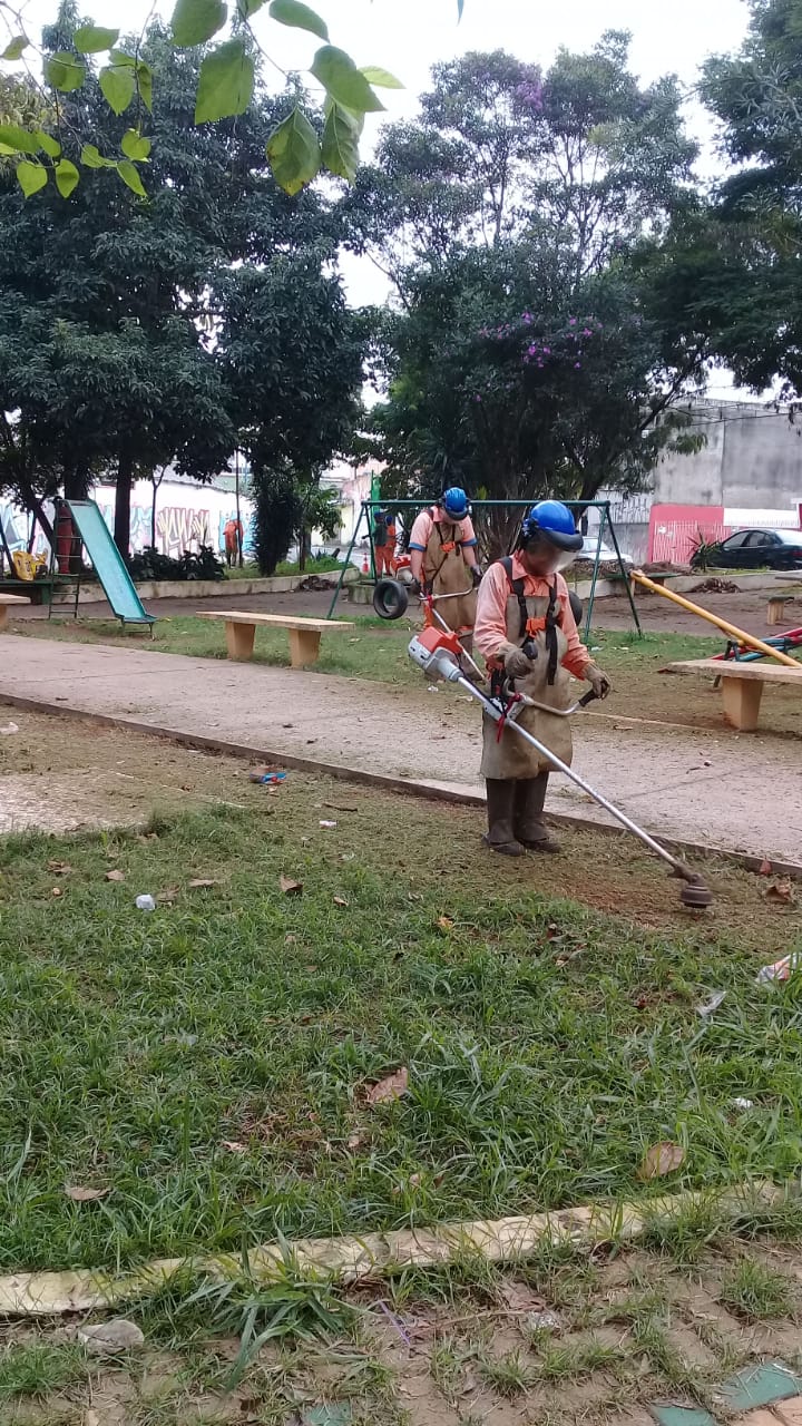 Funcionários na Praça do Costinha podando a grama.
